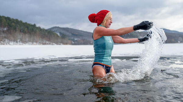 Une femme avec des gants et un bonnet rouge se baignant dans un lac gelé de Slovaquie