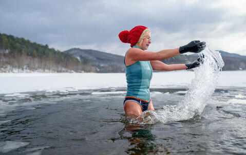 Une femme avec des gants et un bonnet rouge se baignant dans un lac gelé de Slovaquie