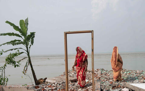 Two women stand on the remains of a house destroyed by erosion on the banks of the Padma River, Bangladesh.