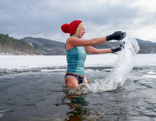 Une femme avec des gants et un bonnet rouge se baignant dans un lac gelé de Slovaquie