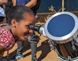 A young Madagascan girl looks the Sun through a telescope