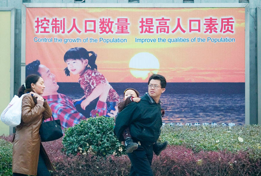 Mother, dad and one child, in front of a propaganda poster promoting the one child per family policy, China