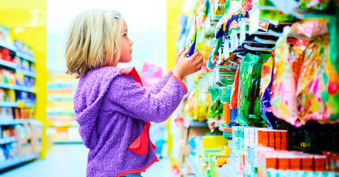 A child blond girl select sweets on shelves in supermarket