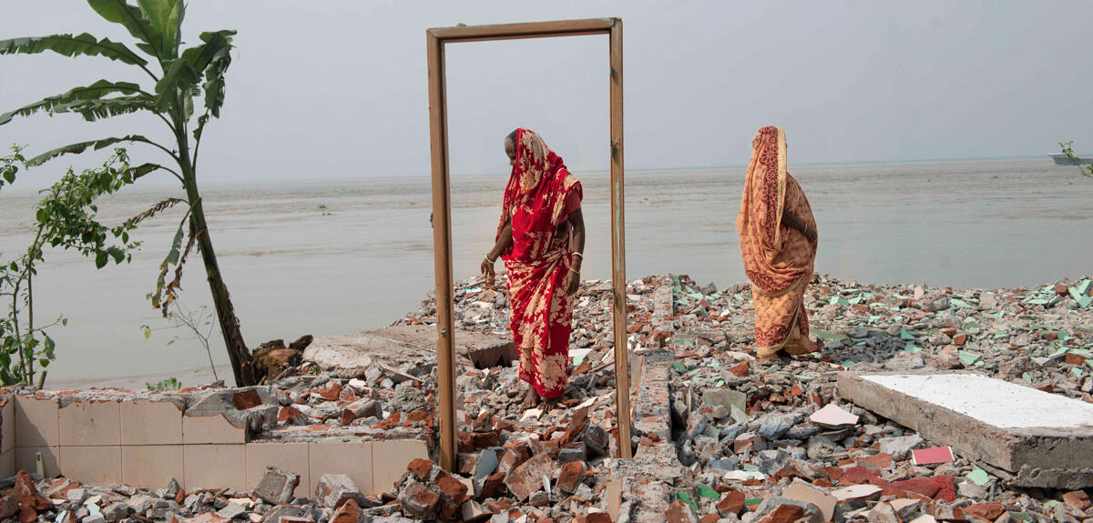 Two women stand on the remains of a house destroyed by erosion on the banks of the Padma River, Bangladesh.